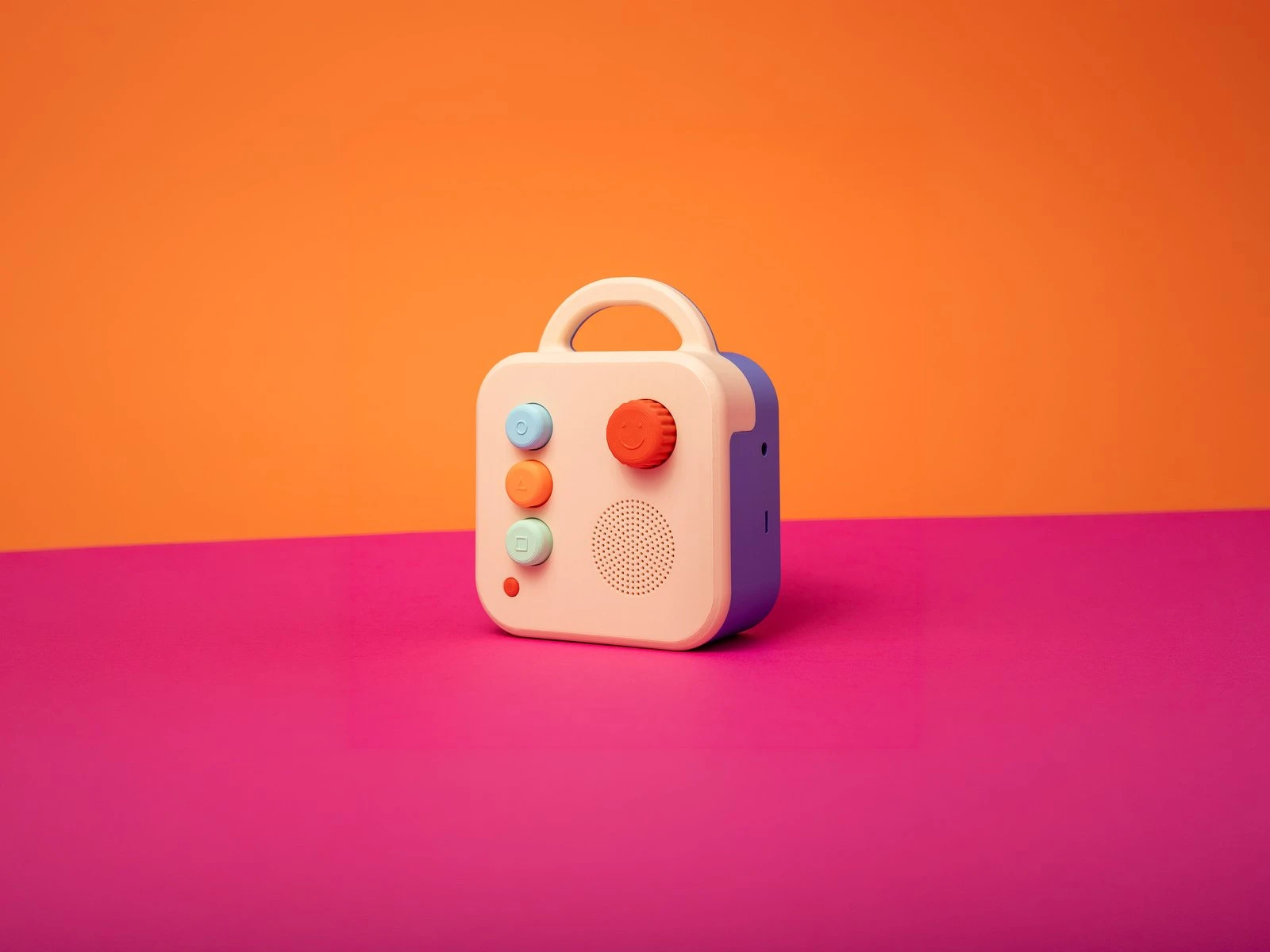 A Koobiba audio player, cream with a purple back and three coloured buttons, on an orange and pink background